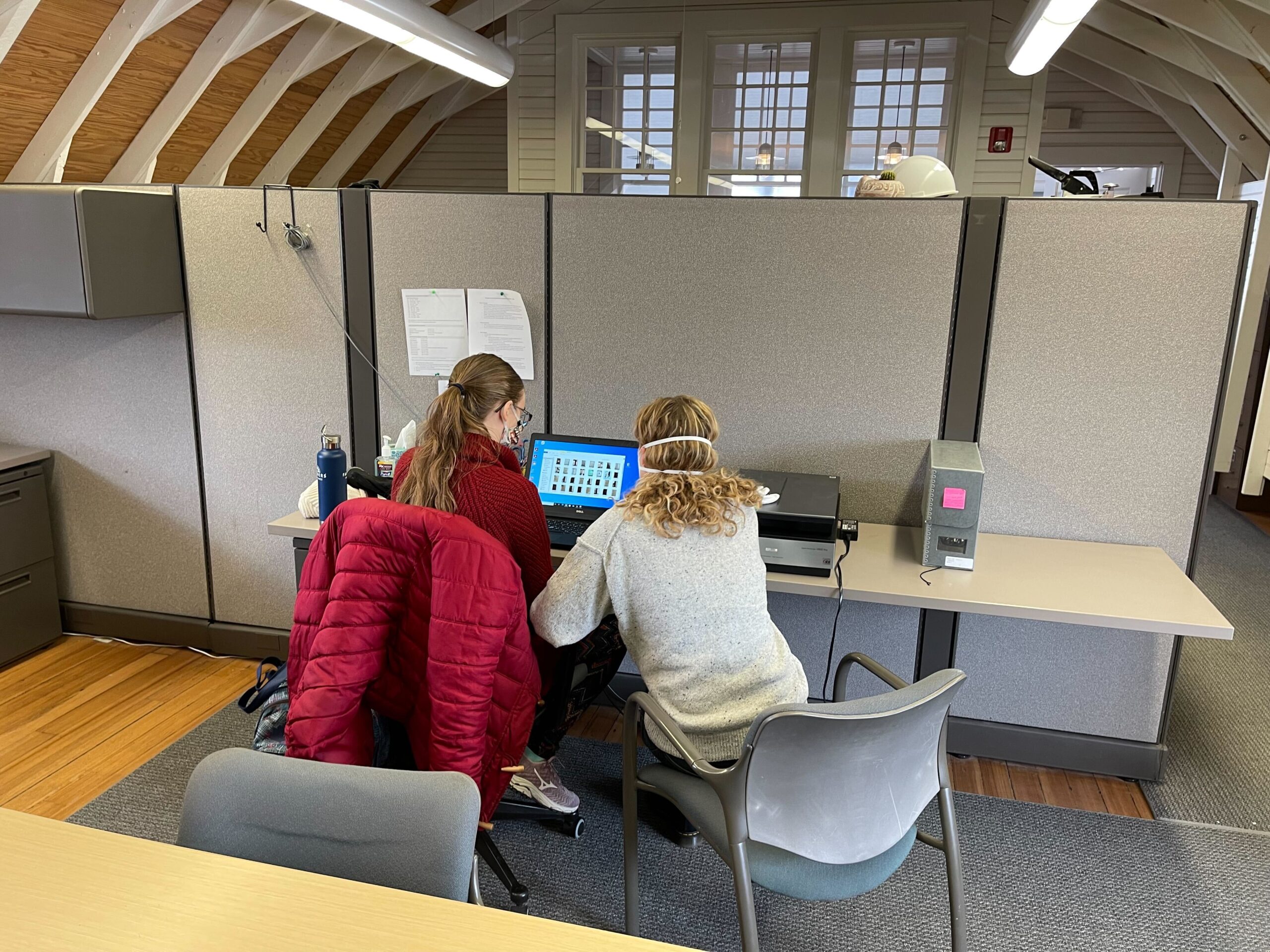 two women sitting at a desk working on a laptop